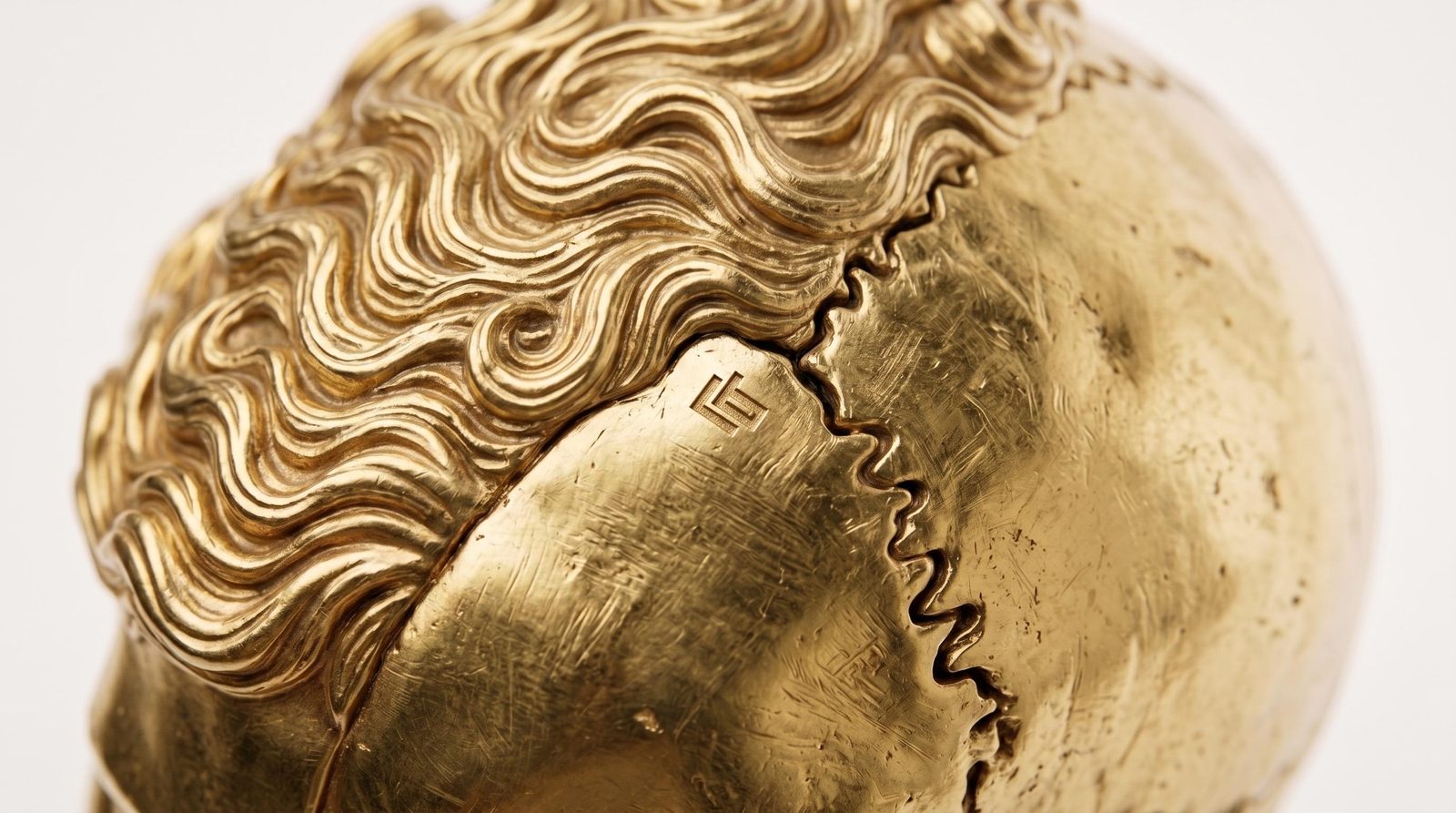 Gold skull crown in close-up — sculpted waves of hair meeting the bare cranium along a toothed suture line